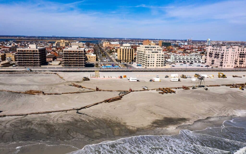 Aerial view of a sandy coastline with a construction site and city buildings beyond