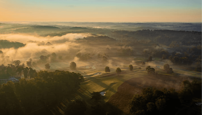 Aerial view of misty farmland and trees at sunrise, with patchwork fields
