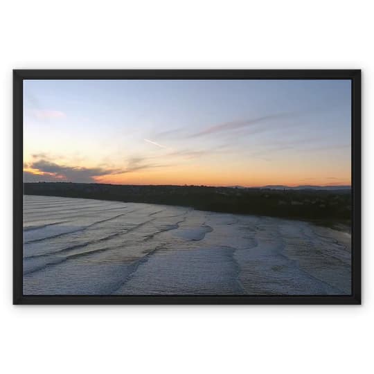 Sunset over a rippled water surface with a distant land silhouette on the horizon