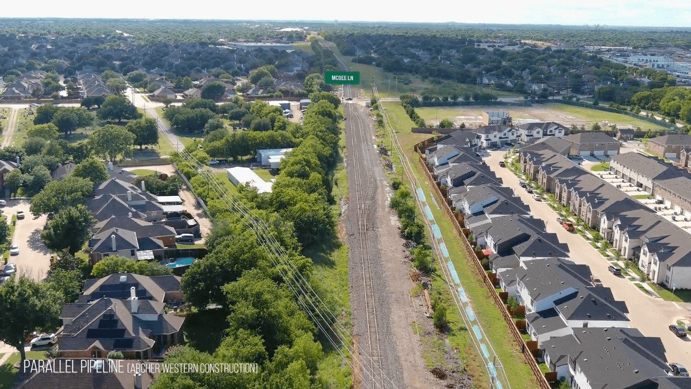 Drone aerial over a railroad between suburban houses, with a green McGee Ln sign above the tracks