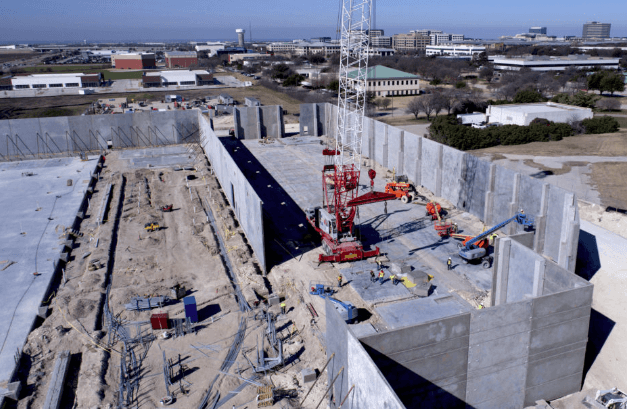 Aerial view of a construction site showing concrete walls, trenches, a red crane, and workers