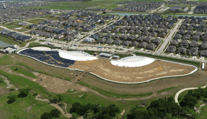 Aerial view of a suburban development with rows of houses and two curved white pool structures