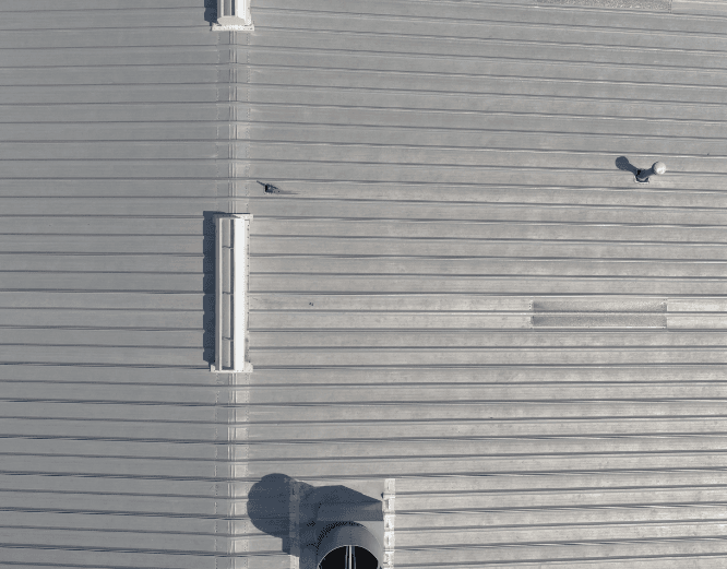 Top-down view of a corrugated metal roof with vents and a small bird on a seam