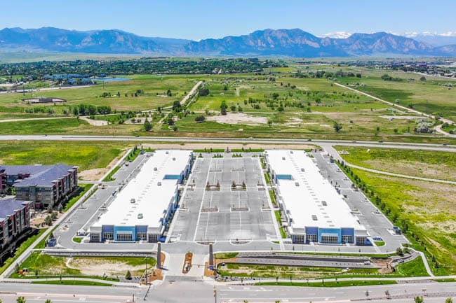 Aerial view of a large industrial complex with white-roof warehouses, parking lots, and distant mountains