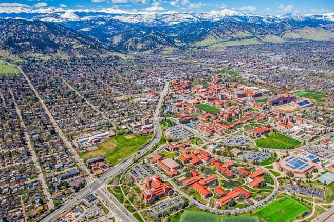 Aerial view of a city with red-roofed buildings, roads, and green fields against mountains