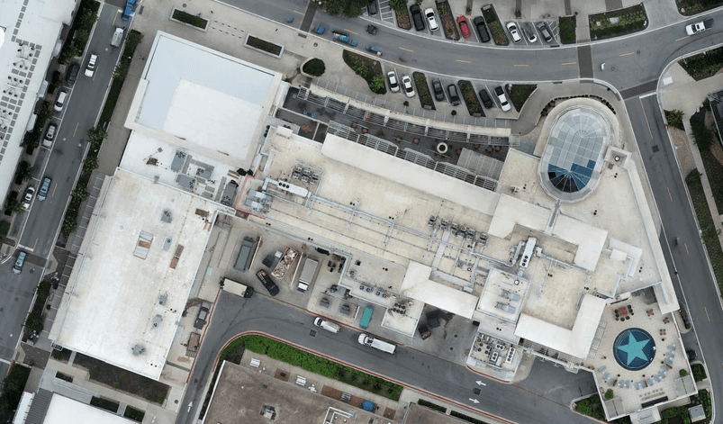 Aerial view of a large white-roof building complex with rooftop equipment and a circular glass skylight