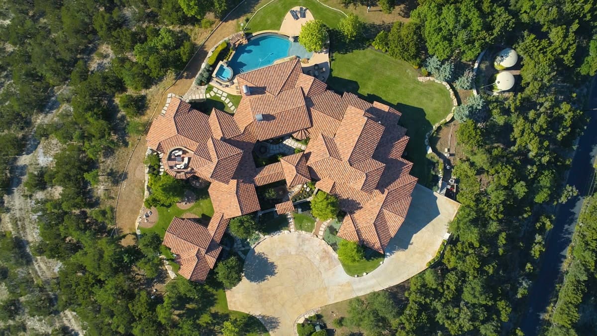 Aerial view of a large red-tiled roof house, circular driveway, pool, and trees