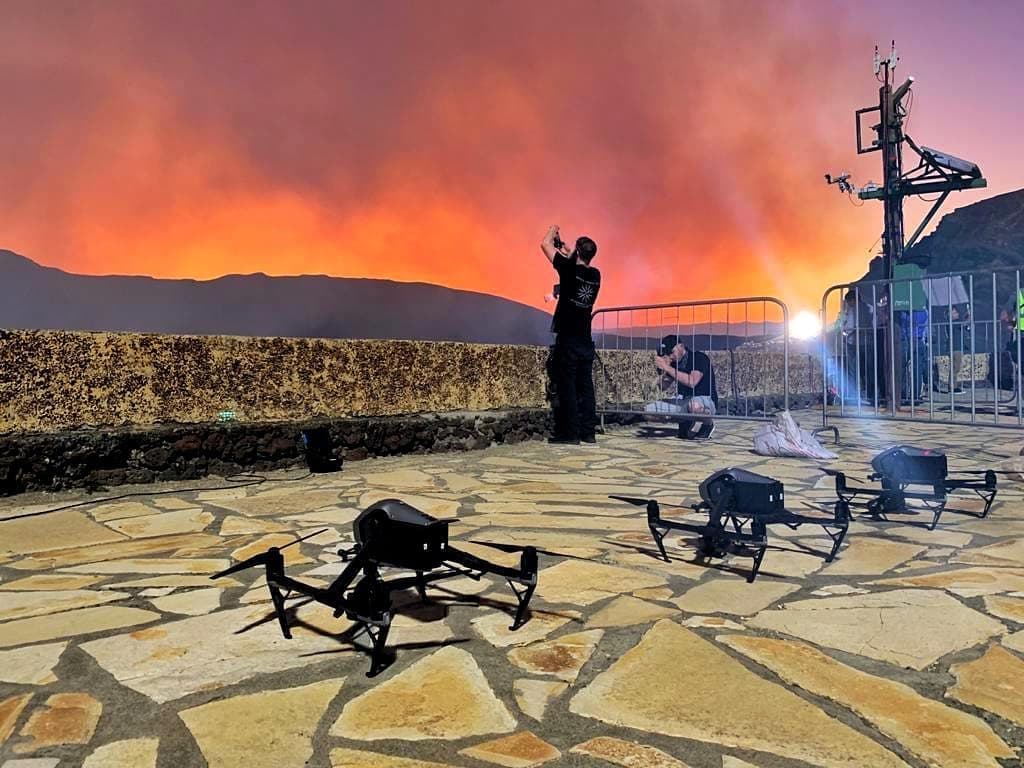 Drones on a stone terrace with an orange sunset; a person shoots photos near a metal barrier