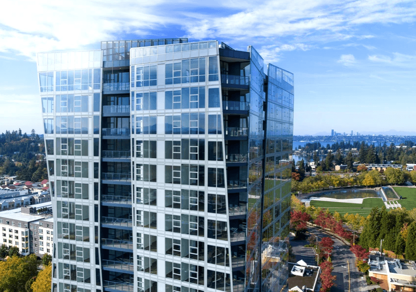 Tall glass-clad high-rise with reflective windows and balconies, urban park in the background