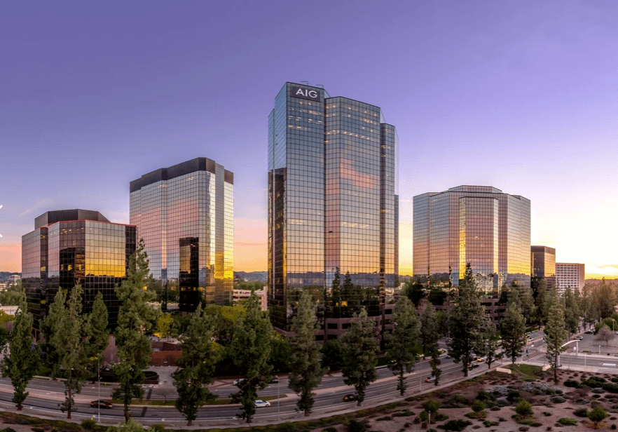 Glass office towers reflect sunset; tree-lined road in foreground and AIG logo on center tower