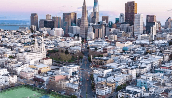 Aerial view of a dense urban skyline with grid streets, tall skyscrapers, and a green field in the lower left