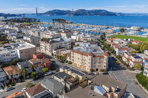 Aerial view of a coastal town with tightly packed buildings, a marina full of boats, and a distant bridge