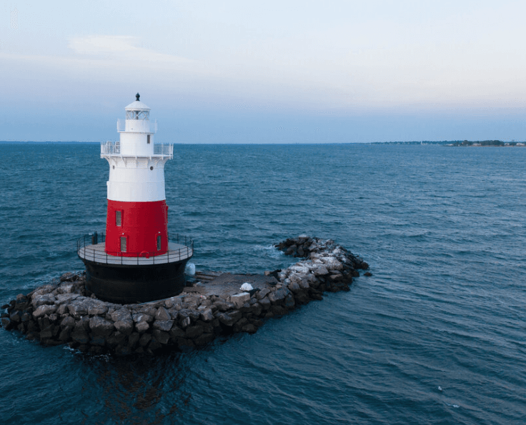 Lighthouse with white top and red lower section on a rocky breakwater in the sea