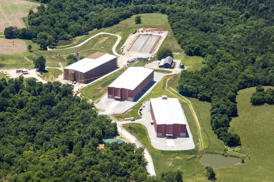 Aerial view of a rural industrial complex with red brick warehouses, white roofs, roads, and trees