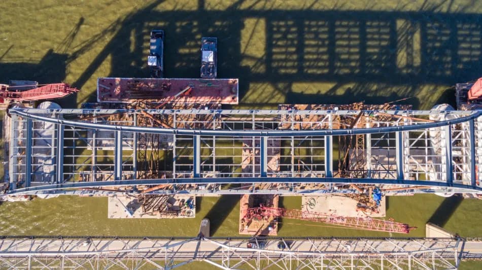Top-down view of a metal lattice tower with scaffolding over green water and construction equipment