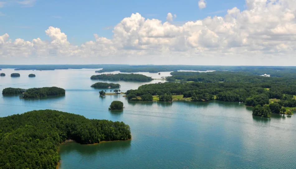 Aerial view of a lake with numerous forested islands and green shorelines under a blue sky with clouds