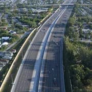 Aerial view of a curved, multi-lane highway on an elevated bridge with vehicles and trees nearby