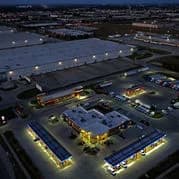 Nighttime aerial view of a commercial complex with simple white roofs, parking lots, and lit streets