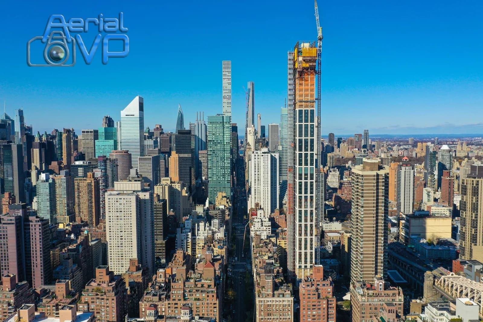 Aerial VP logo over a city skyline with tall buildings and a crane against a blue sky