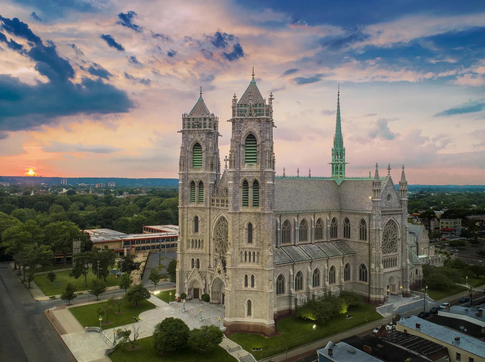 Aerial view of a Gothic cathedral with twin towers and a green spire, stone facade, surrounding trees
