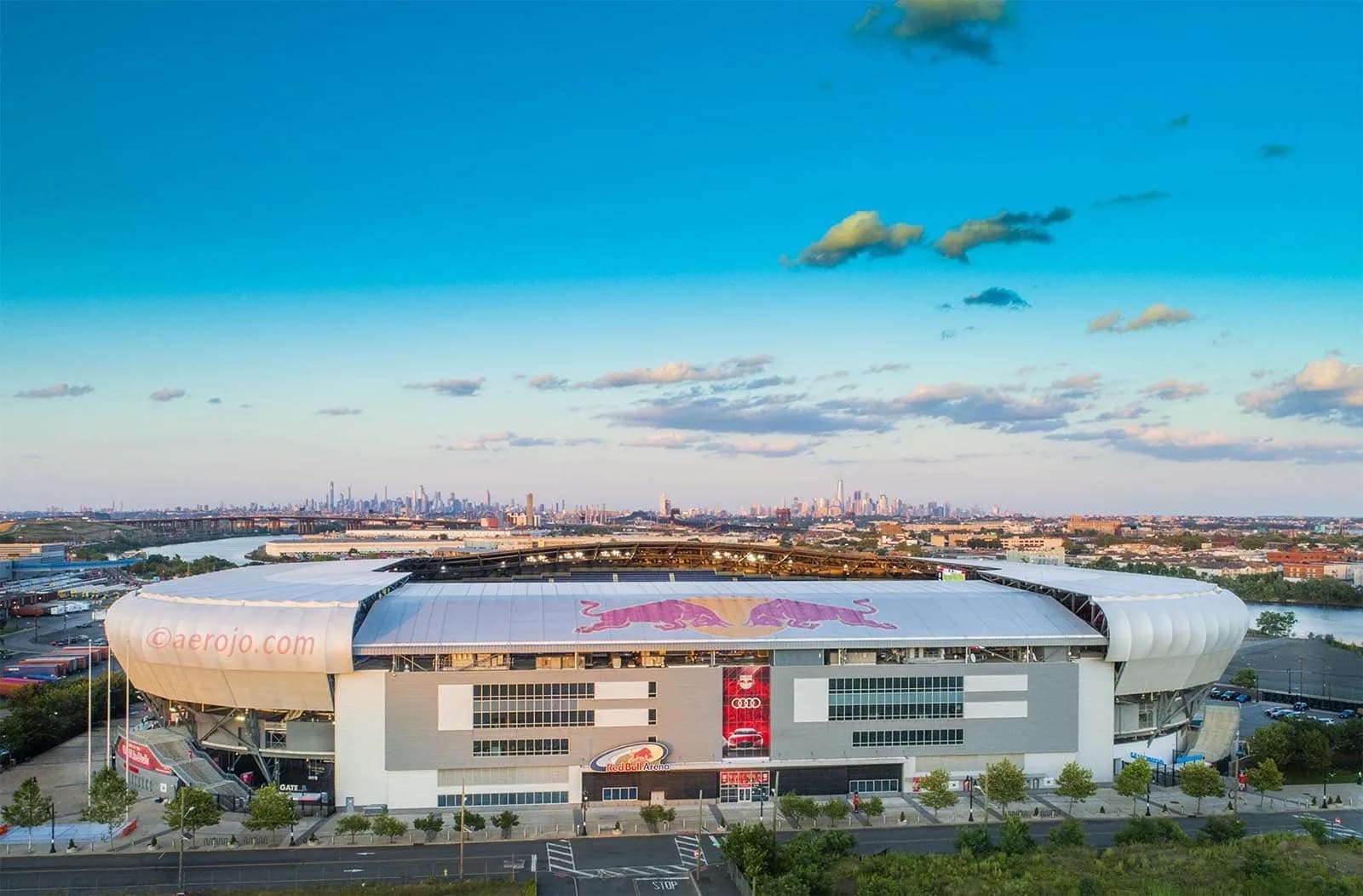 Aerial view of a large stadium with a Red Bull logo on the roof and a distant city skyline