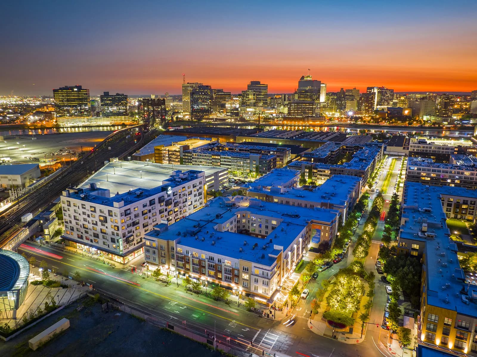 Aerial cityscape at sunset with high-rise skyline, river, and blue-roofed apartment blocks