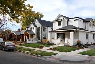 A row of modern white houses on a residential street, with a parked car and autumn trees
