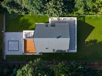 Aerial view of a house with gray roof, a wooden deck on one side, and green lawn with trees