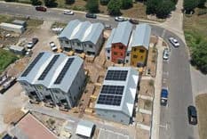 Aerial view of a cluster of gray warehouse buildings, one with solar panels, beside a curved road with cars