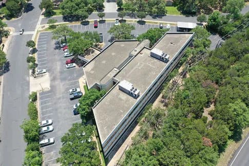 Aerial view of a long, multi-wing building with a parking lot and surrounding trees
