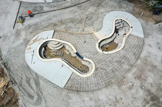 Drone view of a kidney-shaped pool under construction with two connected basins and workers nearby