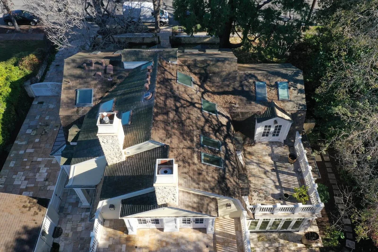 Aerial view of a large house with multiple skylights, chimneys, and a stone patio