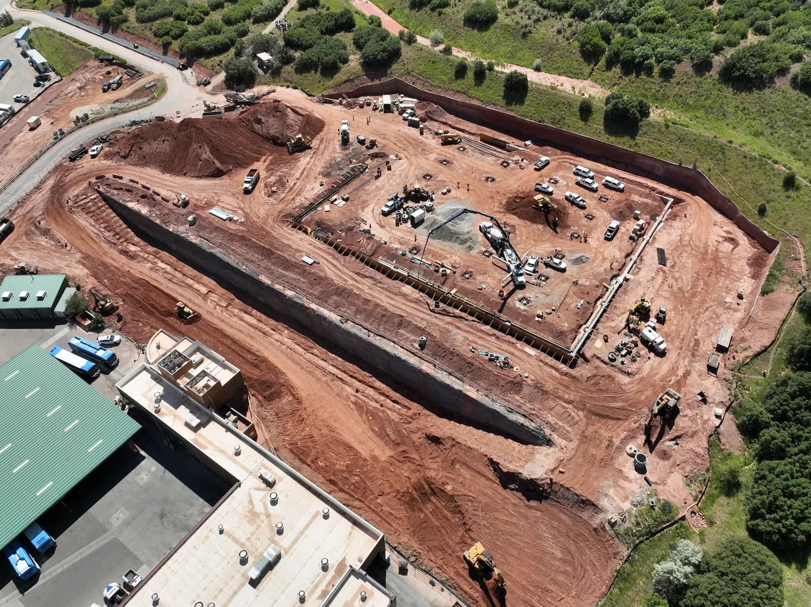 Aerial view of a red dirt construction site with a large excavation pit, machinery, and trucks
