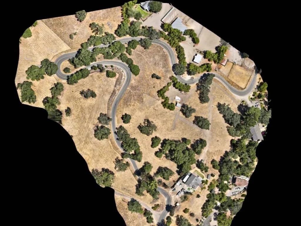 Aerial view of a winding road through a dry hillside with scattered trees and houses
