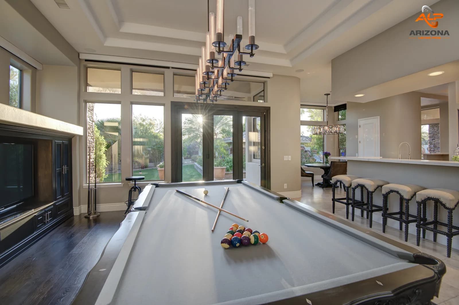 Billiards table in a bright open living area with bar stools and large glass doors to a garden