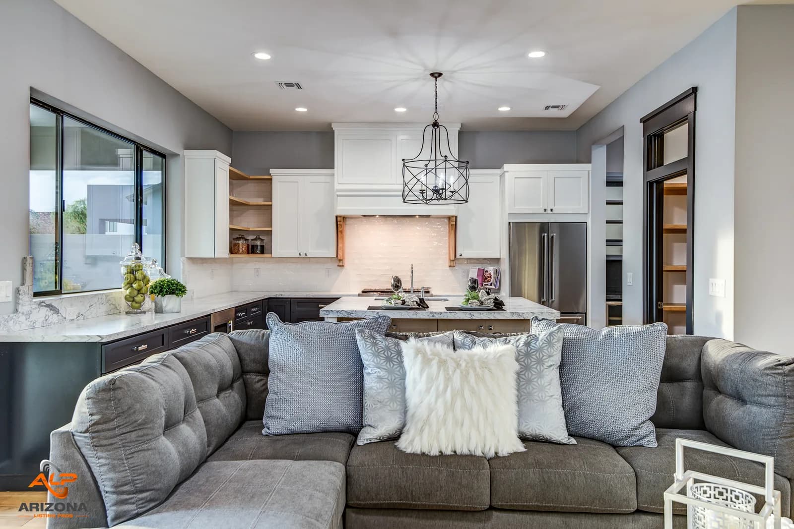Open-plan kitchen and living area with gray sectional sofa, island, and pendant light