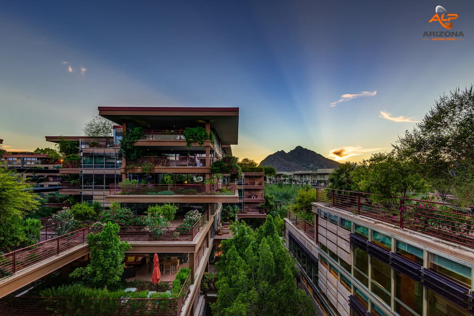 Multi-level terraced apartment complex with rooftop gardens at sunset and a mountain in the distance