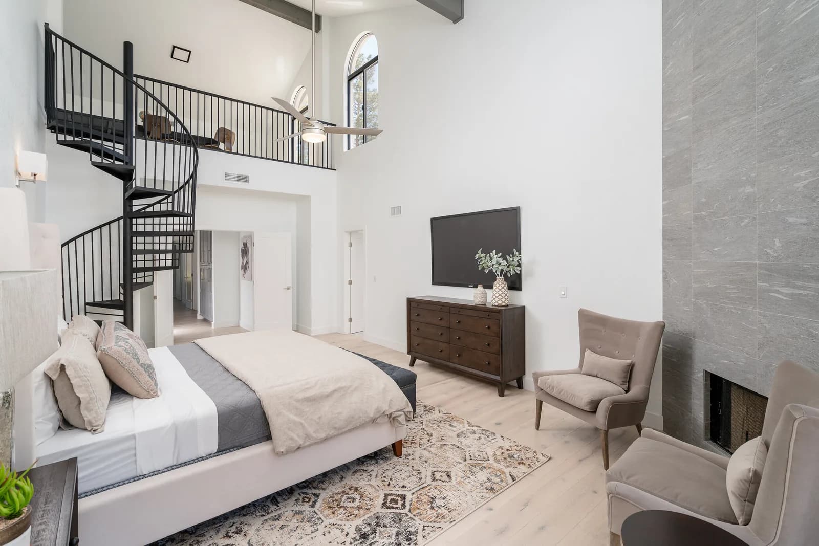 Bright modern bedroom with spiral loft staircase, bed, dresser with TV, and two armchairs