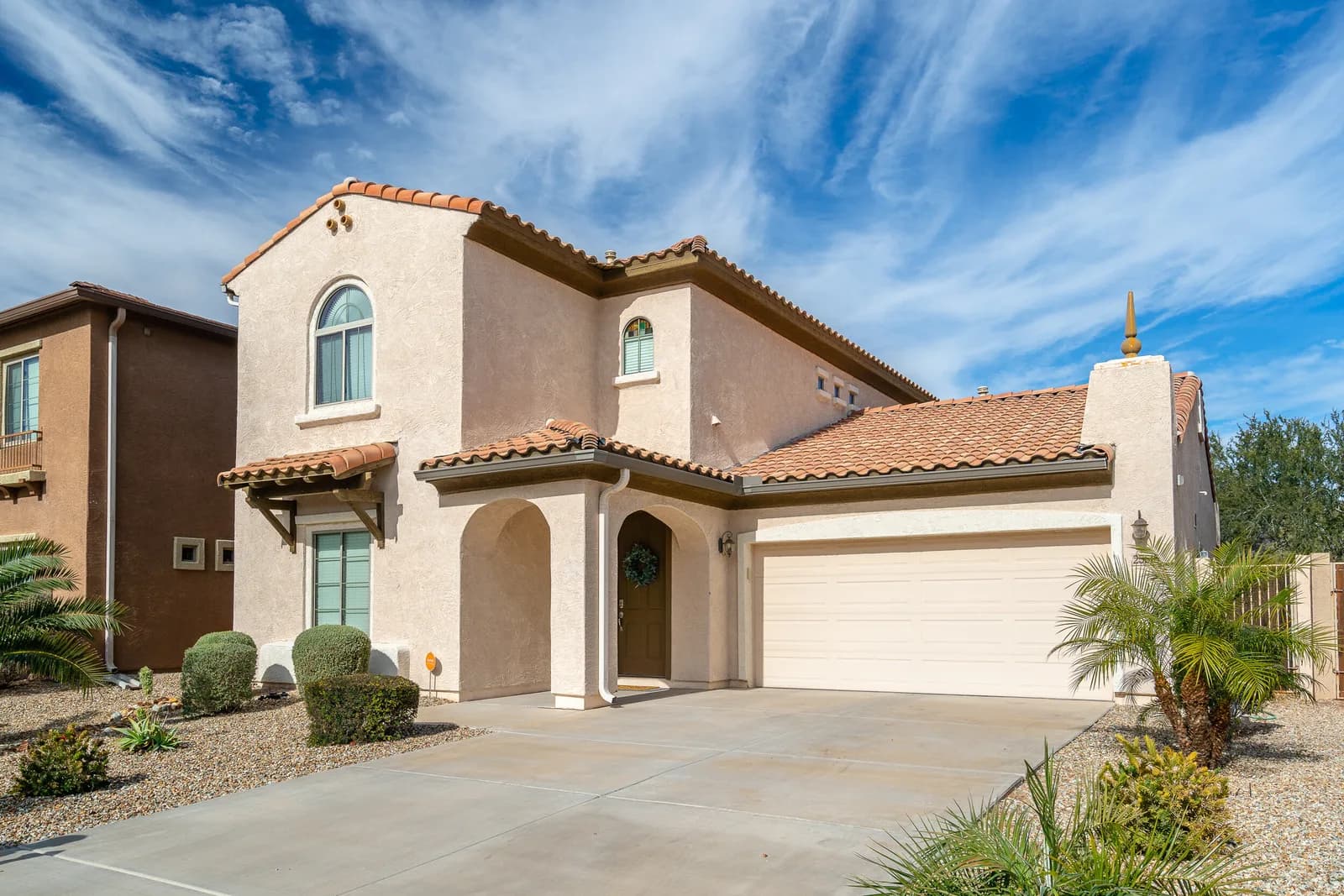 Two-story Mediterranean-style house with terracotta tile roof, garage and desert landscaping