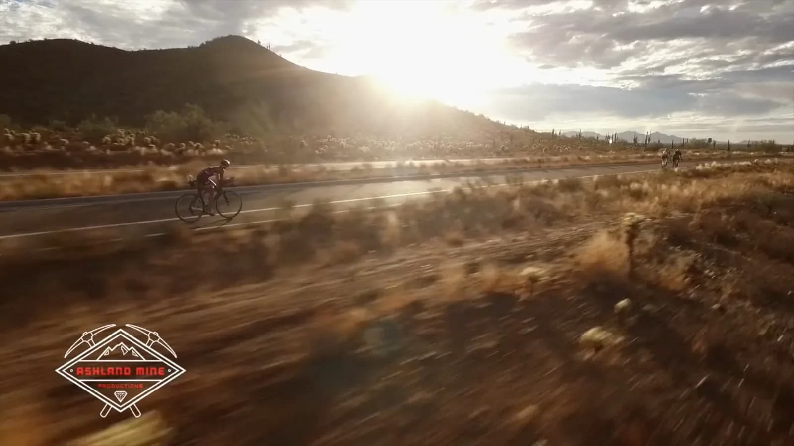 Cyclists riding on a highway at sunset with sunlit desert hills and blurred foreground motion