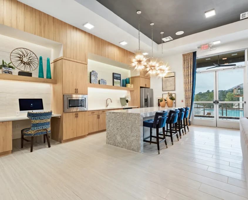 Bright modern kitchen with wooden cabinets, island, bar stools, built-in desk, and glass doors to pool