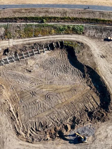 Aerial view of an excavation site with circular tire tracks in dirt and a road above