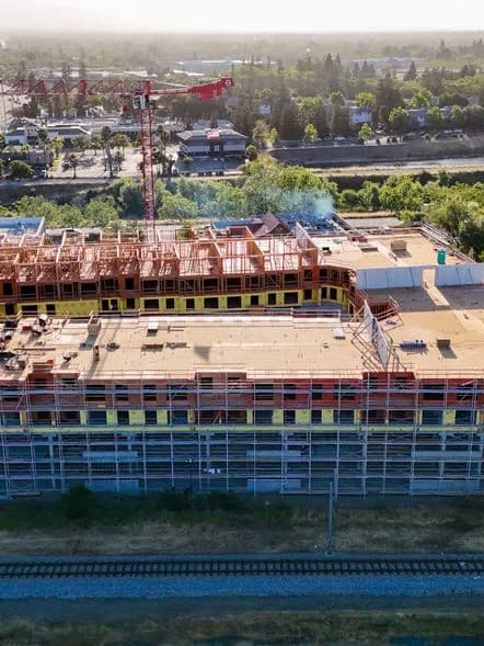 Construction site on a multi-story building with wooden framing and scaffolding, red crane visible