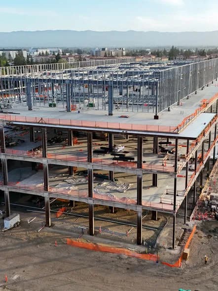 A multi-story steel frame under construction with orange edge barriers and exposed floors