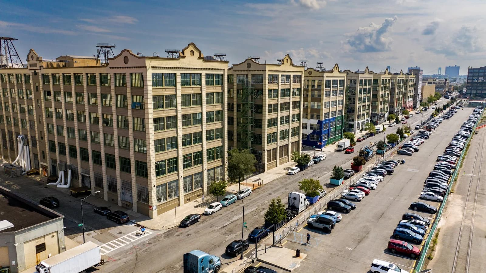 Aerial view of a long row of beige apartment buildings along a street with many parked cars