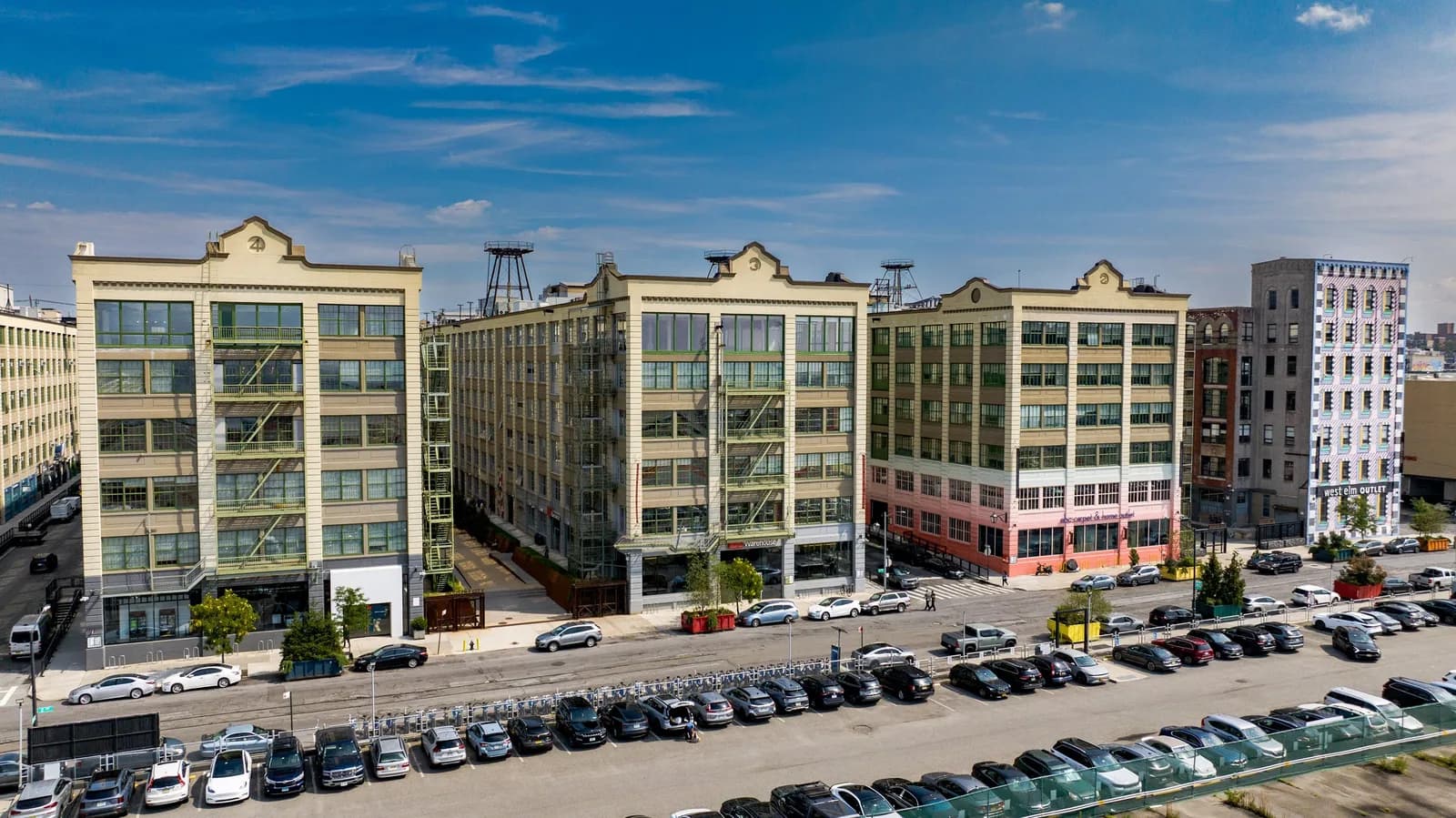 Row of beige mid-rise buildings with large windows along a street, blue sky above, and parked cars
