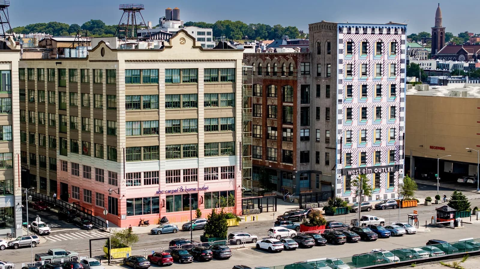 Row of colorful urban buildings along a street, a white building with west elm outlet sign and pink facade