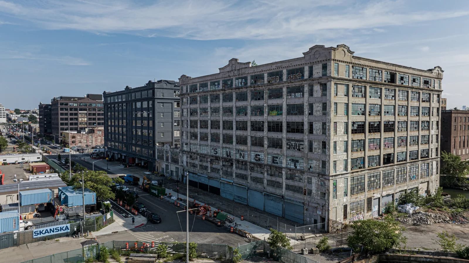 Aerial view of a weathered brick industrial building with many windows, a construction zone and street