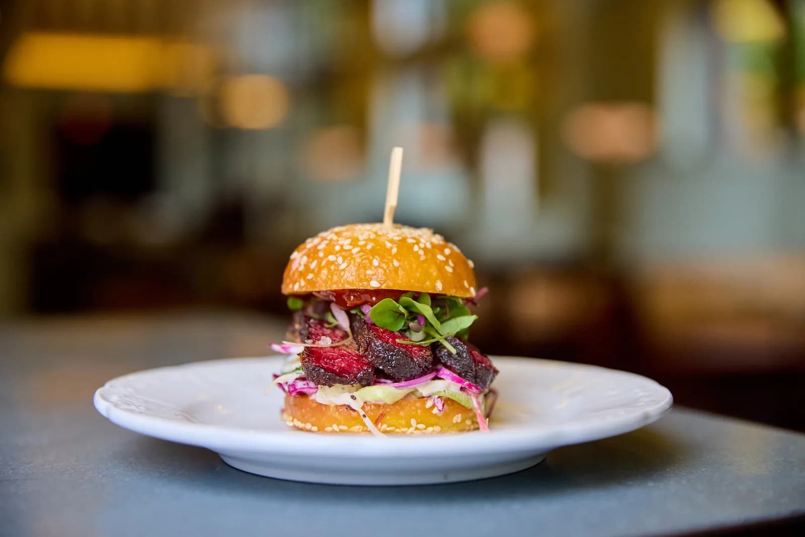 Beef burger with sesame bun, greens, and red onions on a white plate