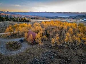 Fall landscape with orange and yellow aspen trees, a dirt clearing and a car, distant mountains
